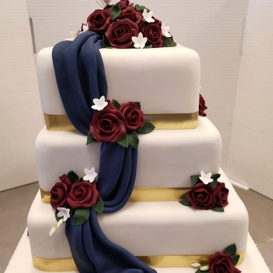 Square three-tier wedding cake with navy drape and red sugar roses
